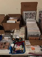 Overview of multiple boxes and containers with alphabet and sentiment stamps, small ink pots, ink pads, and other stamping accessories on a table.