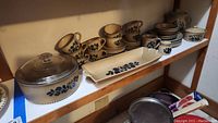 Full view of shelves displaying the Pfaltzgraff pottery set including various cups, bowls, plates, covered casserole and butter dish