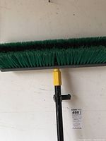 Broom with black and green bristles and yellow connector attached to handle, photo taken to show cleaning tool included.