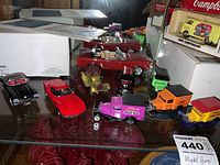 Photo of multiple vintage model cars on a glass shelf including red, black, yellow, purple promotional trucks, and more.