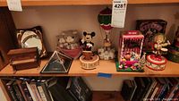 Overview image showing multiple music boxes and figurines on shelves including piano, pyramid, Mickey Mouse, Santa balloon, toy shop, and carolers