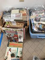 View of baskets and plastic bins filled with vintage needlework magazines, quilting fabrics, and craft supplies.