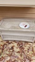 Weathered Suncoast plastic storage box on a wooden deck covered with fallen leaves, showing dirt and wear.