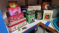 Photo showing overall assortment of metal tins, boxes with vintage-style food branding, and small galvanized pail on shelf.