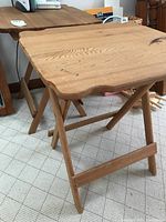 Two wooden center folding TV tables with natural wood finish, showing some stains and scratches, positioned side by side on carpeted floor.