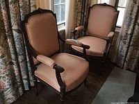 Two peach upholstered antique wood arm chairs in front of window, showing front and side angles