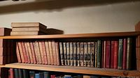 Shelf with various antique hardcover books including burgundy and brown spines with gold embossed text and decoration
