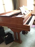 Side view of grand piano showing open lid, carved pedestal leg, and mahogany veneer finish