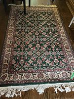 Full view of the Oriental area rug with green central field, floral patterns, and ivory-red-green border.
