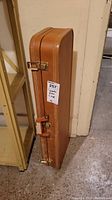 Side view of tan leather long sportsman case showing two brass locks and handle.
