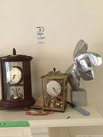 Wide shot showing two clocks and metal sculpture together on a shelf.