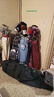 Four upright golf bags with clubs and a black wheeled golf travel bag on floor