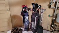 Two golf bags with clubs and two pairs of shoes against basement wall