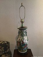 Full view of first hand painted ceramic lamp with floral and bird motifs on wooden base, metal harp and fitting for bulb, no shade.