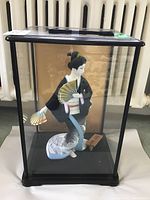 Front view of the Japanese Hakata doll enclosed within the glass display case showing the full doll and part of the case.