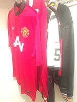 Image showing side view of Manchester United shirt, Mondetta Canada jacket, Winnipeg Jets shirt, Falcons jersey, and Minnesota Vikings jacket hanging together