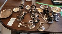 Overview of two multi-arm candelabras, four single holders, scallop dish, small spoons, napkin rings and glass bowl on table.