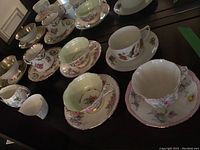 Full assortment of tea cups and saucers arranged in rows, showing detailed floral patterns and gold trim.