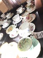 Photo showing nine tea cups and saucers, varied floral designs, gold trim, one mismatched cup and saucer visible