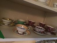 Overview of teacups and saucers arranged on shelf showing different patterns and colors.