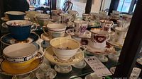 Wide view of multiple fine china teacups and saucers with different patterns and colors.