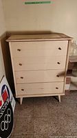 Front view of the vintage wooden dresser showing four drawers with round metal knobs, peeling paint, and standing on tapered legs.
