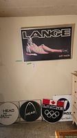 Five unframed signs displayed on floor below framed sign including two Head, one Lange Olympic shield, one Winnwell