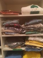 Multiple folded sweaters on white shelving, some in plastic bags