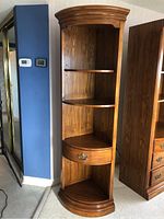 Front view of medium brown oak corner shelf unit with three shelves and a drawer