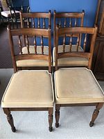 Front view of two wooden dining chairs with spindle backrests and beige padded seats showing wear.