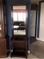 Front view of vintage wooden entry hall stand with full-length mirror and brass coat hooks on each side.