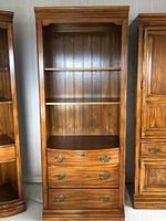 Full front view of oak shelf and drawer unit showing wood grain, shelves and drawers with brass hardware, wood back paneling, decorative molding at top and base.
