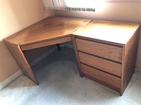 Corner desk and drawer unit set positioned in room corner with window light, showing wood grain top surfaces and general form.