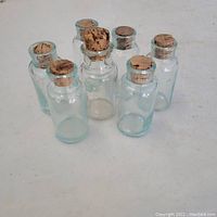 Front view of seven small antique glass bottles with cork stoppers, showing clear and blue glass bottles arranged on a white surface.