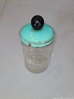 Front view of the antique glass measuring cup with teal blue lid and black wooden knob on top.