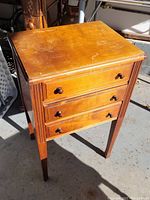 Front and side view of the antique sewing stand showing three drawers and sturdy legs.