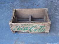 Front view showing the side of the wooden crate with faded green Coca Cola logo and rustic aged wood.