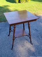 Square solid oak parlor table shown outdoors on pavement with sunlight highlighting wood grain and finish.