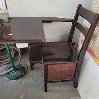 Side view of antique child's wooden school desk illustrating attached chair, desktop with ink well cutouts, and storage drawer below seat.