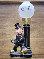 Full side view of vintage ceramic lamp with drunk man figurine leaning on lamp post base with white globe marked 'BAR'