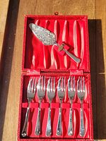 Open view of vintage dessert cutlery set with 6 forks and 1 decorative serving utensil in red satin-lined box.