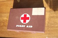 Closed vintage first aid kit plastic case with red cross logo and 'FIRST AID' label on lid.