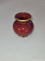 Front and side view of small reddish-brown glazed pottery vase with gold rim on neck and base.