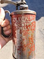Close-up of the front body showing worn red paint, rust, and white stamped lettering 'GOLDEN MFG CO' and 'OMAHA, NEBR'.