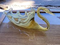 Side view showing the swan shape with its curved neck and shallow bowl body in amber-colored glass.