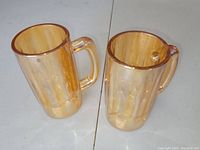 Two golden oxen carnival glass beer mugs placed side by side on a white surface, showing front and handle