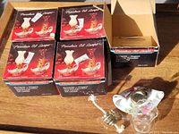 Five boxed miniature porcelain oil lamps, some boxes open showing lamp components including glass chimney and brass burner with wick.