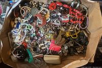 Top-down view of box filled with assorted older costume jewelry showing variety and colors