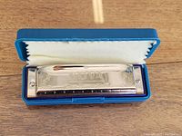 Harmonica in open blue plastic case showing shiny silver body with brand engraving and markings