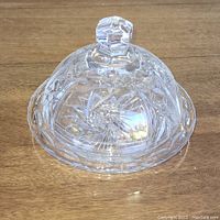 Crystal butter dish dome cover with faceted knob sitting on wood surface